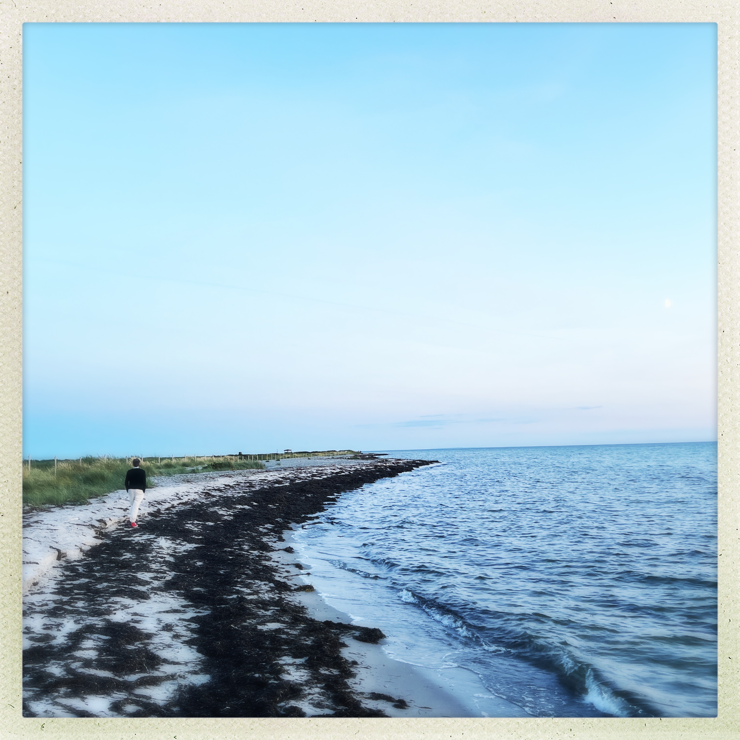 Person som promenerar längs stranden i skymning